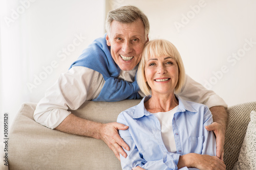 Lovely mature man embracing wife and smiling to camera