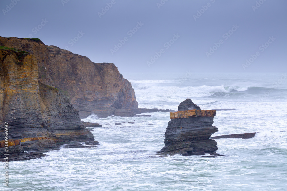 A huge ocean waves breaking on the coastal cliffs in at the cloudy stormy day. Breathtaking romantic seascape of ocean coastline. Peniche, Portugal.