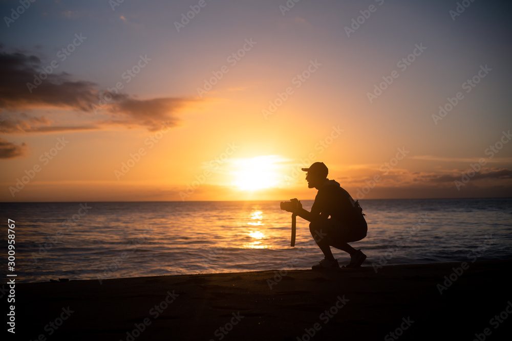 Obraz premium The silhouette of a male hobbyist photographer taking photos of a beautiful colorful sunset on the West Puerto Rico coast near Rincon