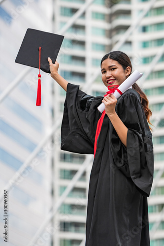 A female Asian student in graduation gown holding the diploma and graduation cap photo