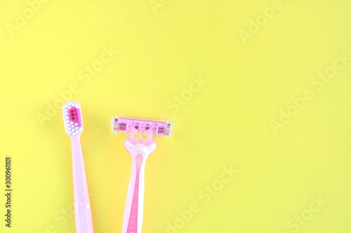 pink disposable razor for safe shaving of female skin and toothbrush with selective focus on yellow background. Woman Razor and toothbrush on bright backdrop. Sharp razor for personal hygienic routine