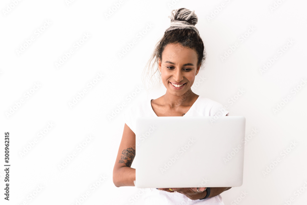 Cheerful happy smiling young african woman with dreads posing isolated over white wall background using laptop computer. Cheerful happy smiling young african woman with dreads posing isolated over white wall background using laptop computer.