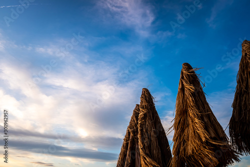 Cloudy background with at sunset with three palm tree umbrellas at a holiday resort.