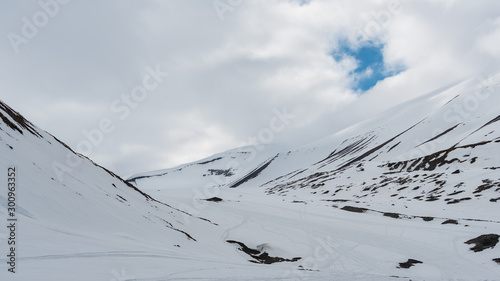 Snow covered mountains in cloudy weather with snowmobile tracks and small patch of blue sky