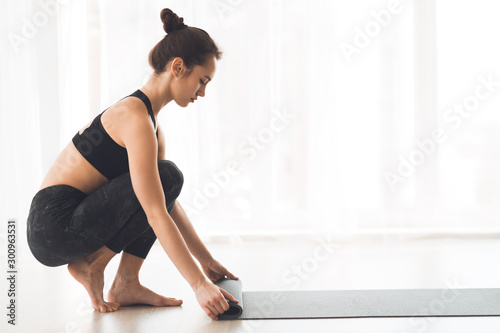 Sporty woman rolling mat after yoga class