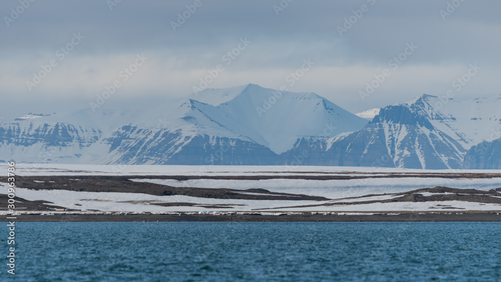Landscape of distant snow covered mountains behind the rocky shore of an arctic fjord in Svalbard