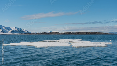 Blocks of ice floating in an arctic fjord on a sunny day with blue sky and snowy mountains in the distance in Svalbard