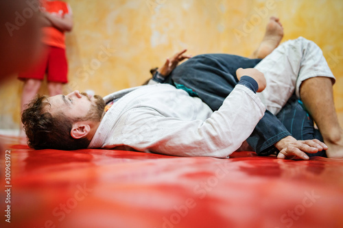 Brazilian jiu jitsu BJJ brown belt athlete or instructor demonstrating technique on his student during the training or sparring at the academy drill guard position