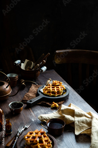baked waffles with maple syrup or honey on wooden boards stands on rustic table
