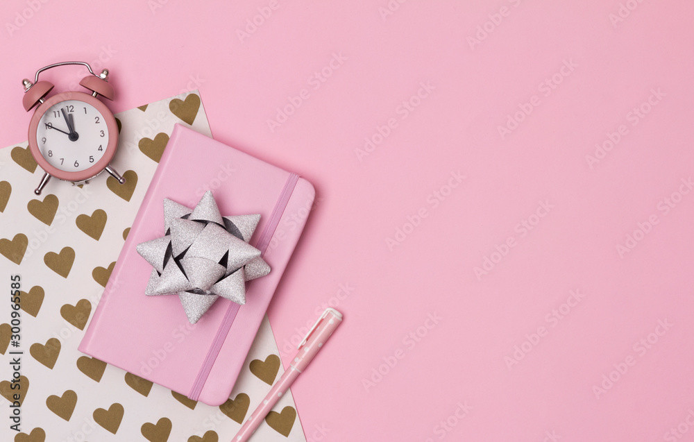 Pink notepad with alarm clock, bow and pen on creative background Pink notepad with alarm clock, bow and pen on creative background