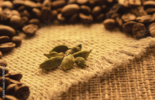several cardamom beans on burlap against a background of coffee beans
