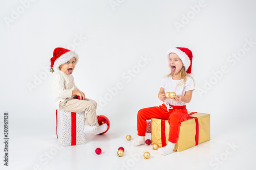 Happy little kids in Santa hat with Christmas gift boxes showing wheir tongues, white background. Holidays, christmas, new year, x-mas concept. © Olga