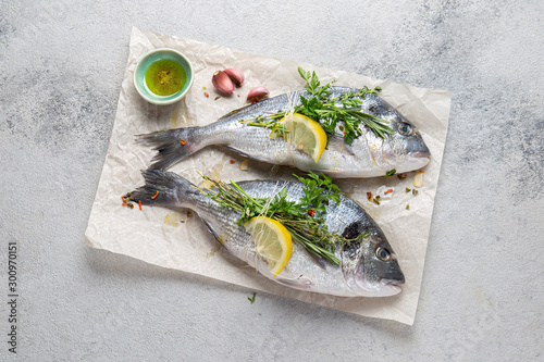 Dorada fish, raw fresh sea bream with lemon and herbs on a grey stone background, top view.