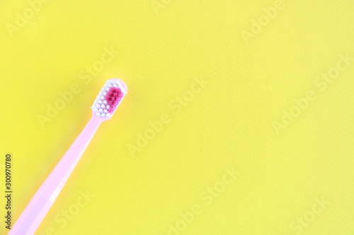 Pink Toothbrush with colorful bristles in bright yellow background with empty space for text. Teeth hygiene concept. Toothbrush for personal healthcare. 