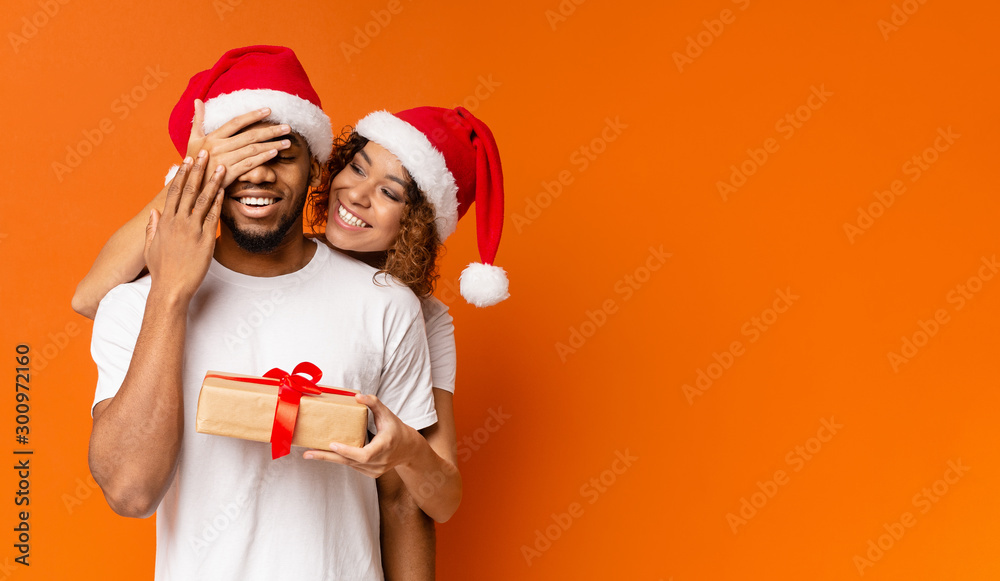 Black millennial couple with Christmas gift on orange background - obrazy, fototapety, plakaty 