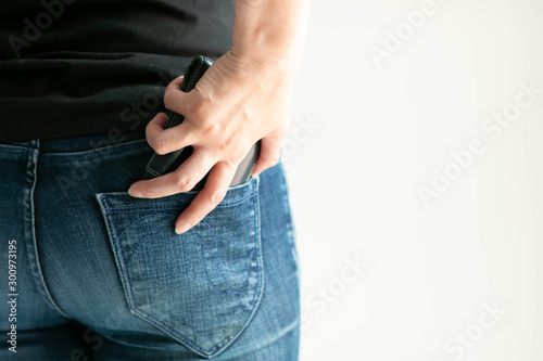 A woman keeps a short wallet in the back pocket of jeans on a white background with copy space.