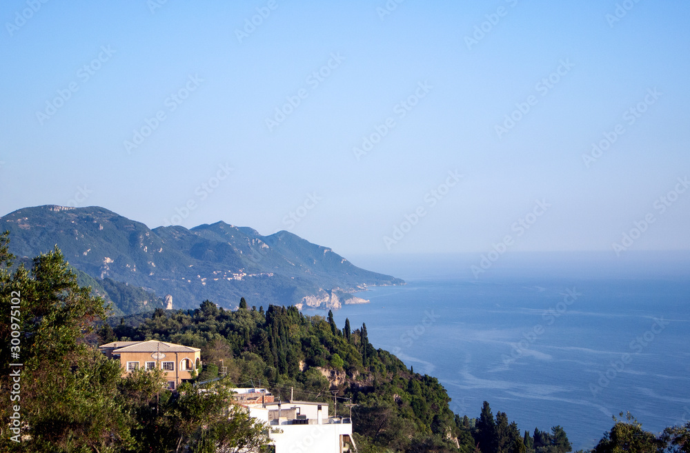 Pine clad cliffs and high hills by the Ionian sea on the Greek island of Corfu. A verdant green landscape with a view down the coast to distant bays and coves.