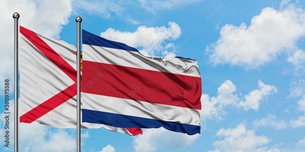 Jersey and Costa Rica flag waving in the wind against white cloudy blue sky together. Diplomacy concept, international relations.
