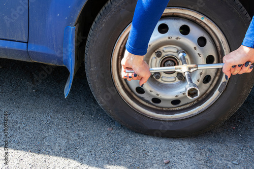 Beautiful girl with the cylinder key changes the wheel in the broken car. Replacement tires on the side of the country road. Car insurance concept