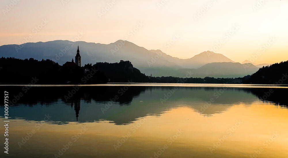 Sunrise at Lake Bled Slovenia and its reflection. Symmetry is the concept. Alps in background. Tower of bell church in the island is visible.