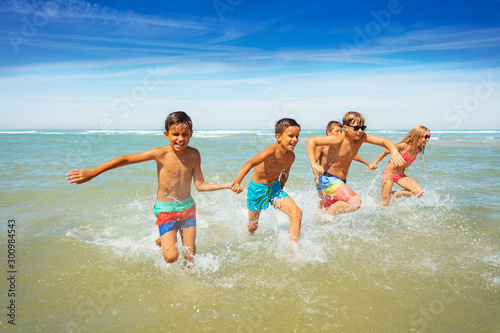 Many boys and girls run in ocean waves on a beach