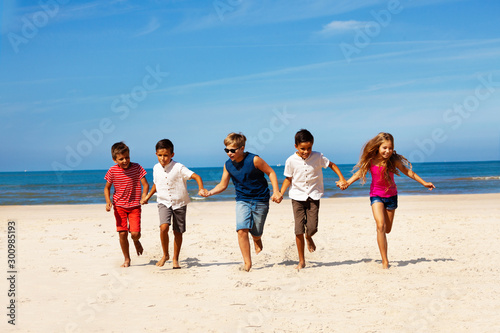 Many children run together holding hand on a beach