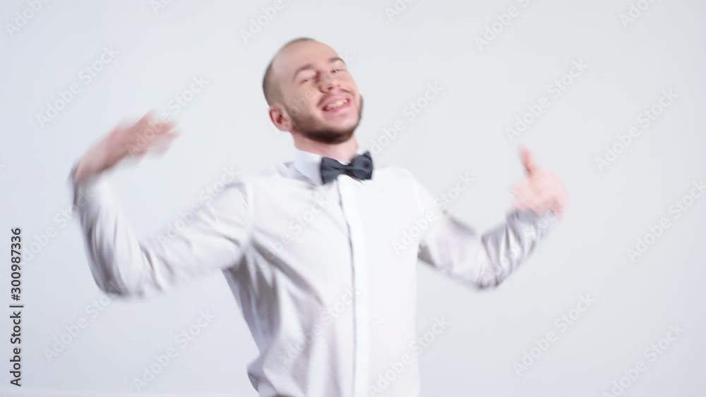 Portrait shot of happy man in white shirt and bowtie smiling and dancing isolated on grey background Portrait shot of happy man in white shirt and bowtie smiling and dancing isolated on grey background