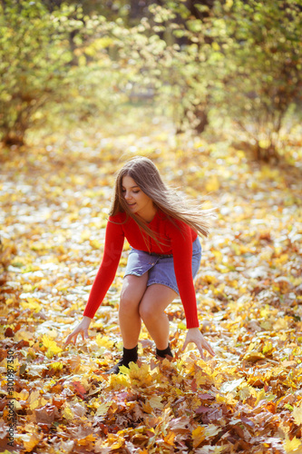 Happy girl throws up autumn leaves in park for walk outdoors.