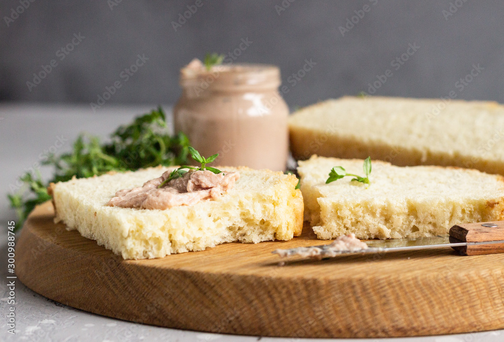 Fresh homemade chicken liver pate on bread with thyme on a wooden cutting board. 