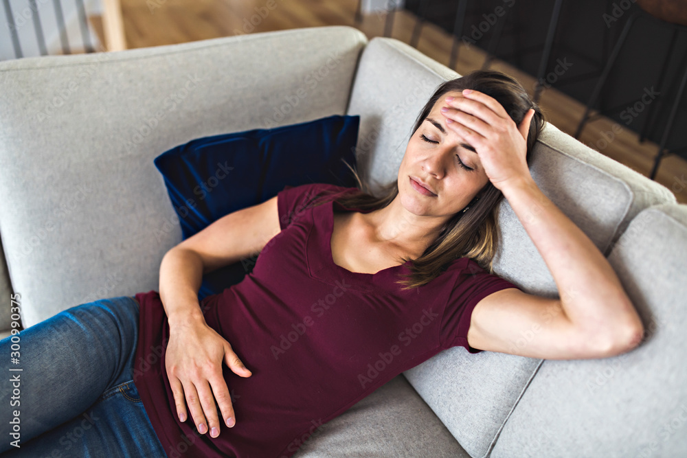 Obraz premium A Sick woman lying on sofa in the living room with stomach ache