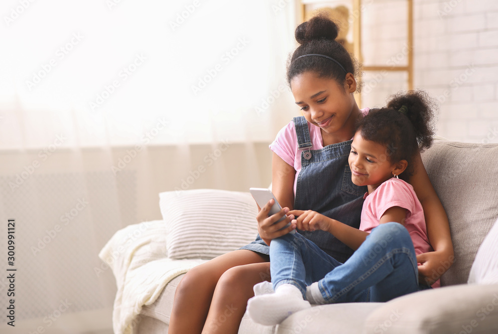 Cheerful african sisters using cellphone at home Cheerful african sisters using cellphone at home
