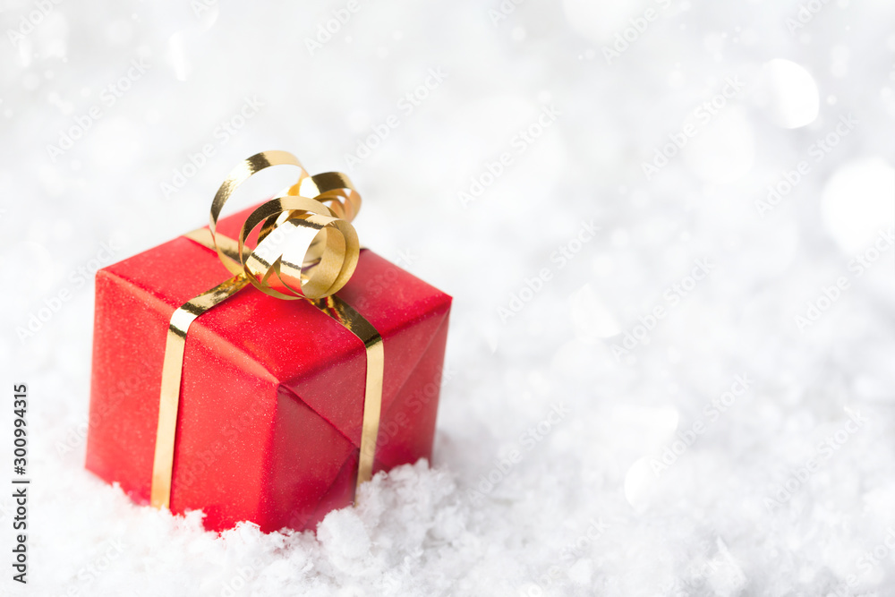 Red gift box with golden bow in snowdrift. Christmas and New Year greeting card with place for text. Red gift box with golden bow in snowdrift. Christmas and New Year greeting card with place for text.