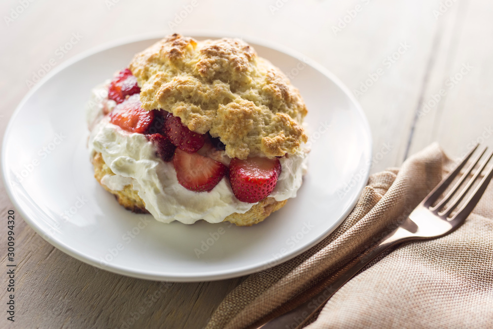 One strawberry shortcake on a white plate with fresh whipped cream, shown with fork and cloth napkin. 