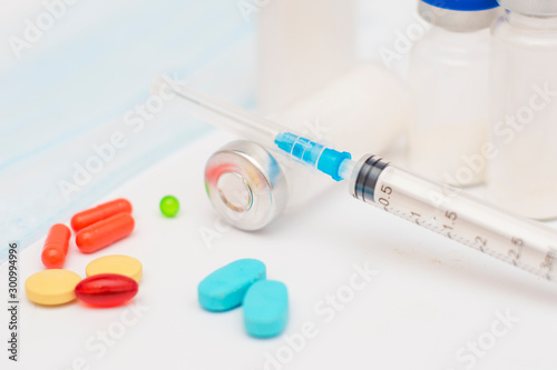 Tablets of different shapes and colors and a syringe with an antibiotic and a vaccine on a white background. Medical concept.