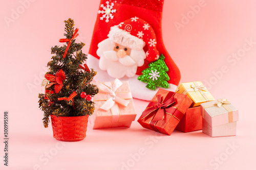 Christmas concept. Decorated Christmas tree with four gift boxes on a pink background. Gift sock in the background.