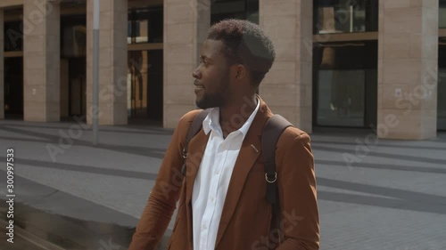 Tilt down of smiling stylish African man driving to work by electric kick scooter along street in city center