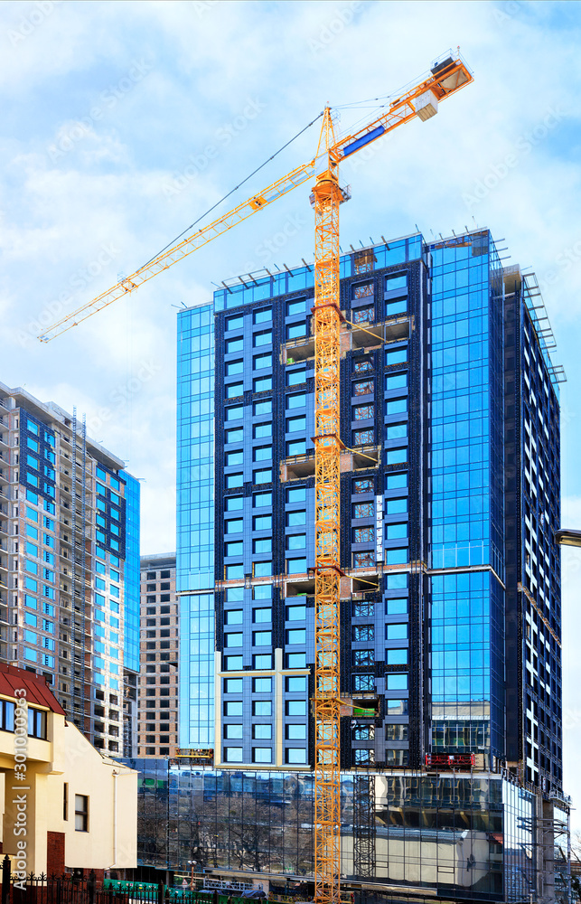 The glass facade, a reflection of the blue sky and crane near a modern concrete building under construction.