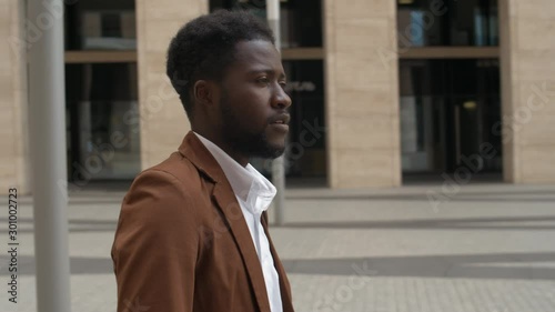 Panning of African businessman wearing trendy casual clothes using modern e-scooter and looking around in city center