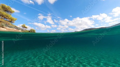 Above and below underwater photo of tropical exotic turquoise sandy beach in Caribbean secluded destination with deep blue sky and clouds