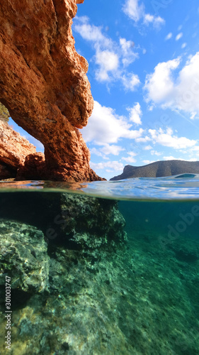 Above and below underwater photo of tropical exotic island arch cave with emerald sea and deep blue sky