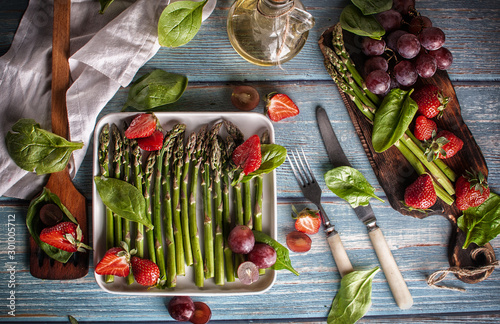 green asparagus with strawberries, bread, grapes. on a white plate on a blue table