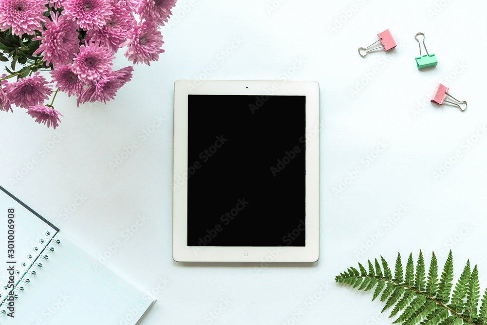 Tablet computer, notebook, paper clips, bouquet of pink chrysanthemums and fern leaves on a white background. Cozy workplace, top view, copy space. Tablet computer, notebook, paper clips, bouquet of pink chrysanthemums and fern leaves on a white background. Cozy workplace, top view, copy space.