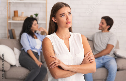 Offended Girl Standing While Boyfriend Flirting With Girl Sitting Indoor