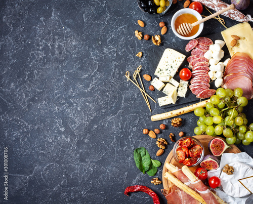 Italian antipasto with prosciutto, ham, cheese, olives and grissini breadsticks on black stone background.