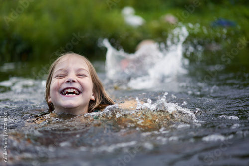 Girl clumsily swims in a small pond near the shore.