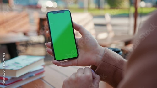 Young hands woman holding use phone with green screen sitting in cafe scrolling pages swiping surfing internet technology smartphone chroma key message close up slow motion