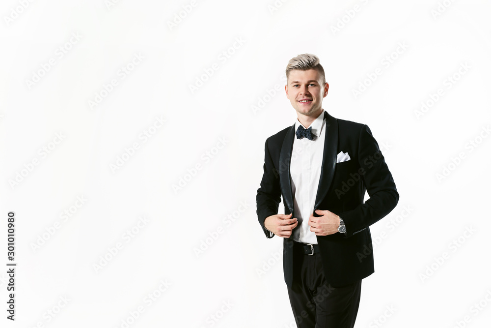 Portrait of young smiling handsome man in tuxedo stylish black suit, studio shot isolated on white background. Showman or toastmaster in jacket with bowtie Portrait of young smiling handsome man in tuxedo stylish black suit, studio shot isolated on white background. Showman or toastmaster in jacket with bowtie
