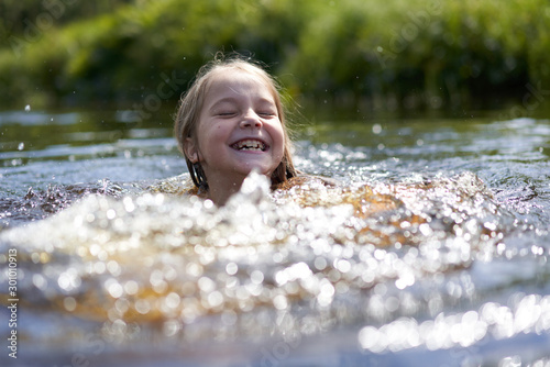 Girl clumsily swims in a small pond near the shore. photo