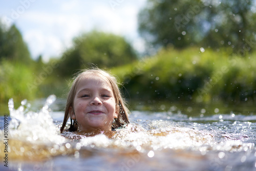 Girl clumsily swims in a small pond near the shore.