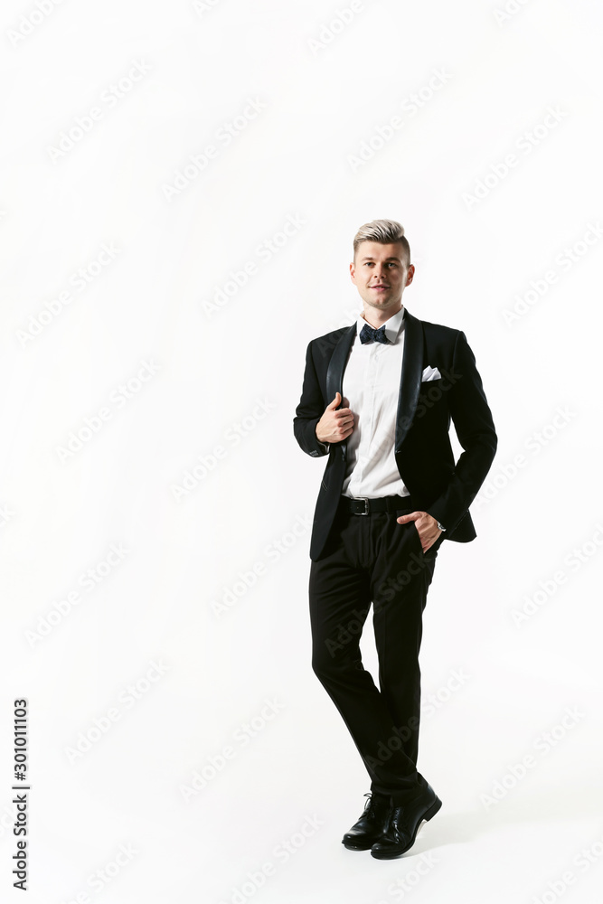 Portrait of young smiling handsome man in tuxedo stylish black suit, studio shot isolated on white background. Showman or toastmaster in jacket with bowtie Portrait of young smiling handsome man in tuxedo stylish black suit, studio shot isolated on white background. Showman or toastmaster in jacket with bowtie